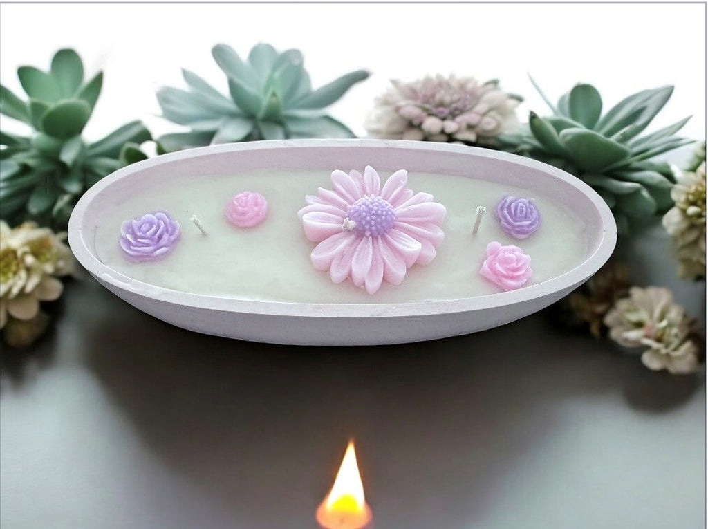 Oval white dish candle with pink daisy and purple rosebuds surrounded by succulents